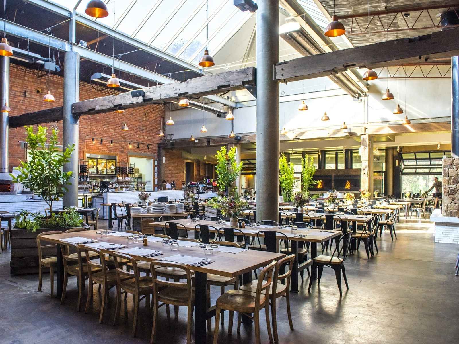 Spacious interior of The Epicurean Red Hill showcasing long timber tables, skylights, and lush greenery — an elegant and flexible setting for funerals or celebrations of life in Red Hill.