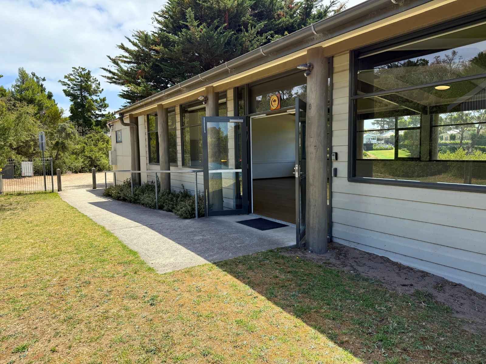 Side entrance with open door, concrete path and railings, surrounded by trees.