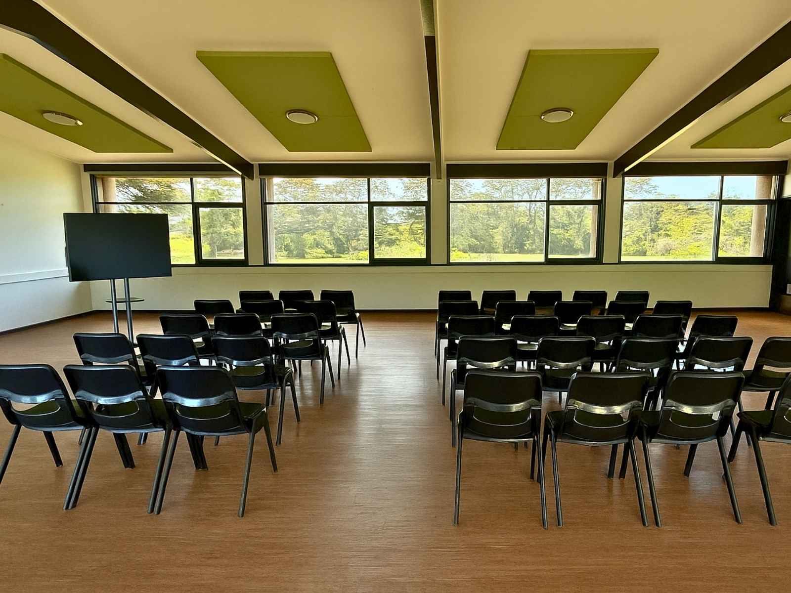 Interior setup with rows of black chairs facing a screen, surrounded by large windows and natural light.