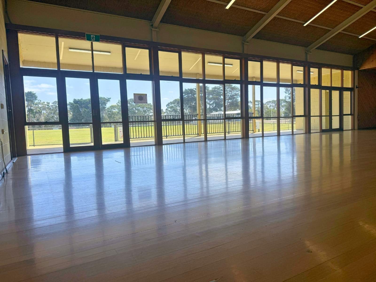 Unfurnished view of the main hall space, showing polished floorboards and natural light through large windows.