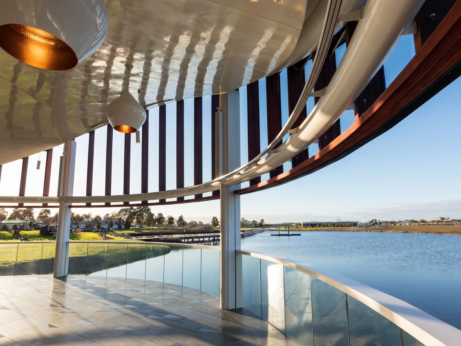 Curved open-air veranda at Sanctuary Chapel, Bunurong Memorial Park, with pendant lights overlooking the lake
