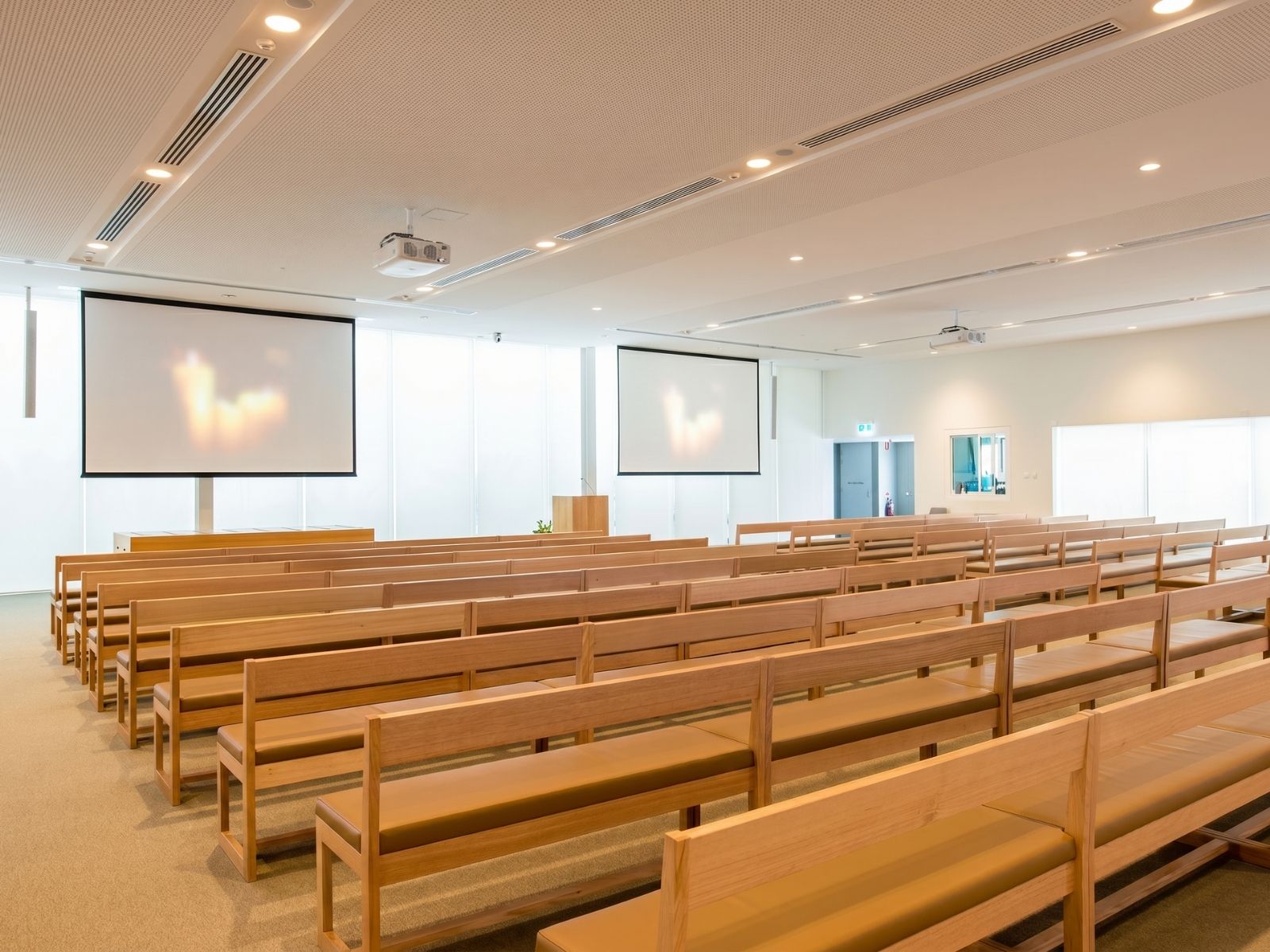 Rows of timber pew seating and twin projection screens inside Stratus Chapel at Bunurong Memorial Park