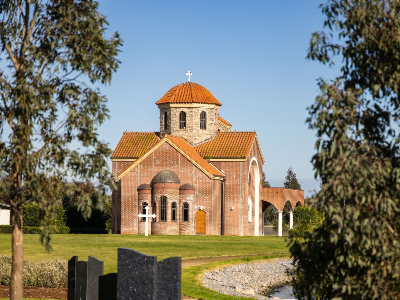 Saint Lazarus Greek Orthodox Church at Bunurong Memorial Park framed by eucalypts, with memorial headstones in the foreground