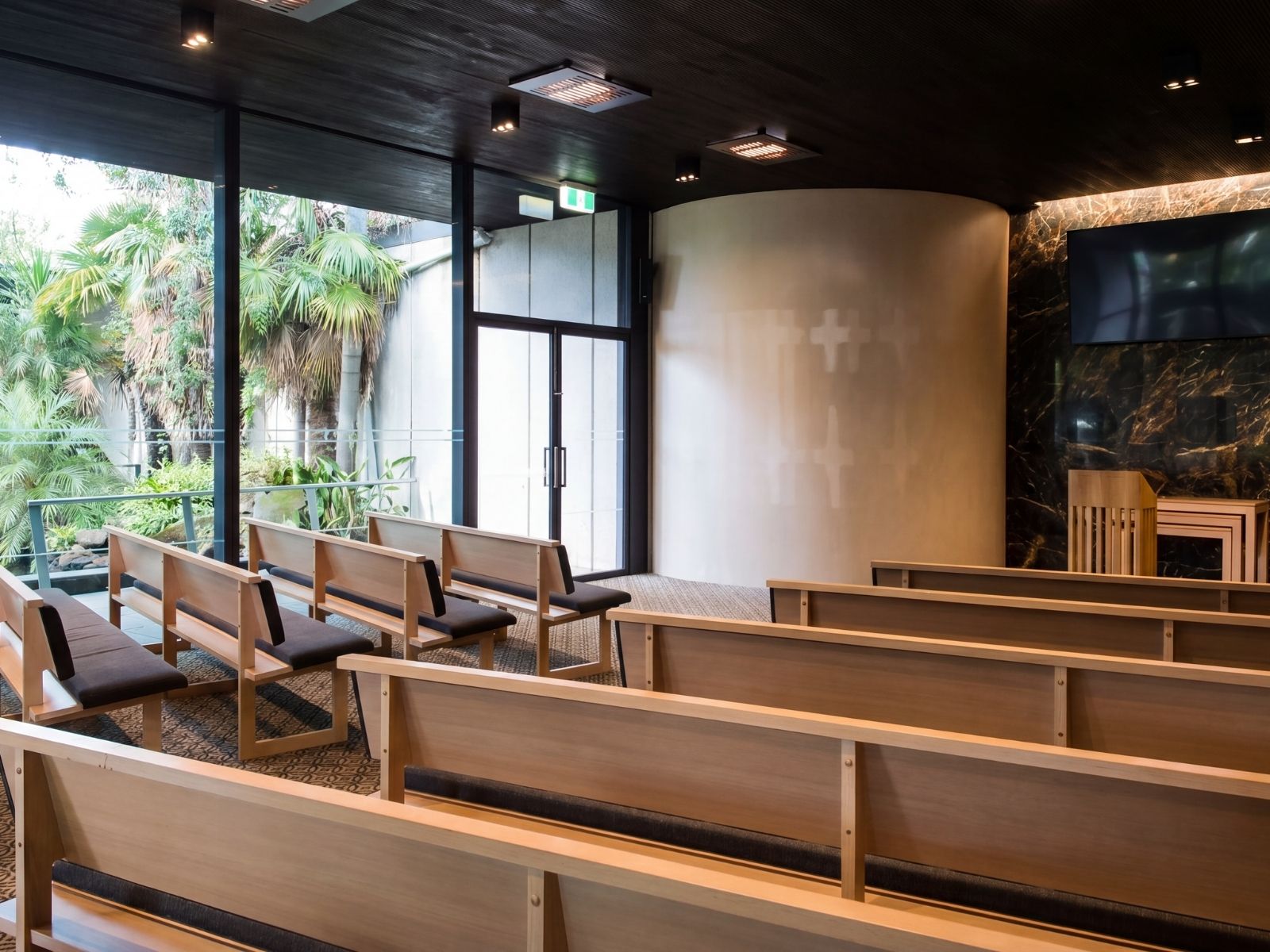 Timber pews and curved catafalque wall inside Blair Chapel at Springvale Botanical Cemetery