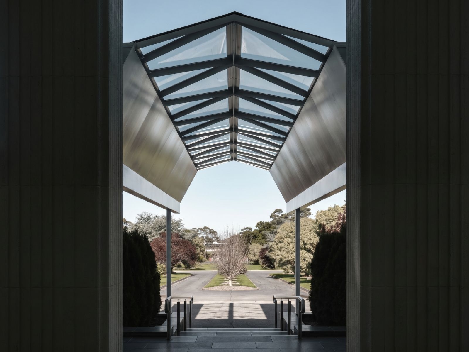 Folded steel porch canopy at the Atrium entry, framing the view down the cemetery avenue