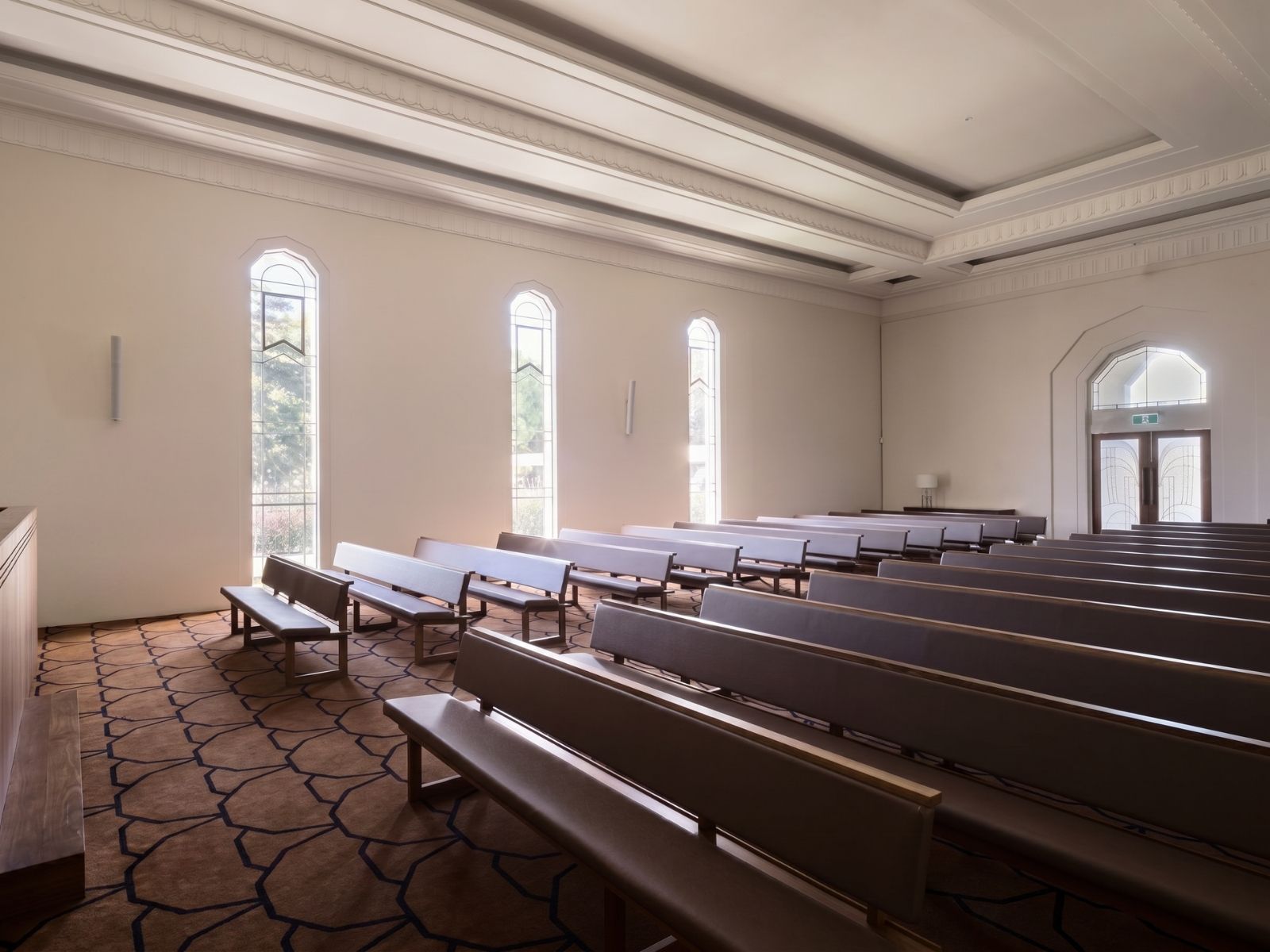 Boyd Chapel interior with dark timber pews beside tall arched leadlight windows