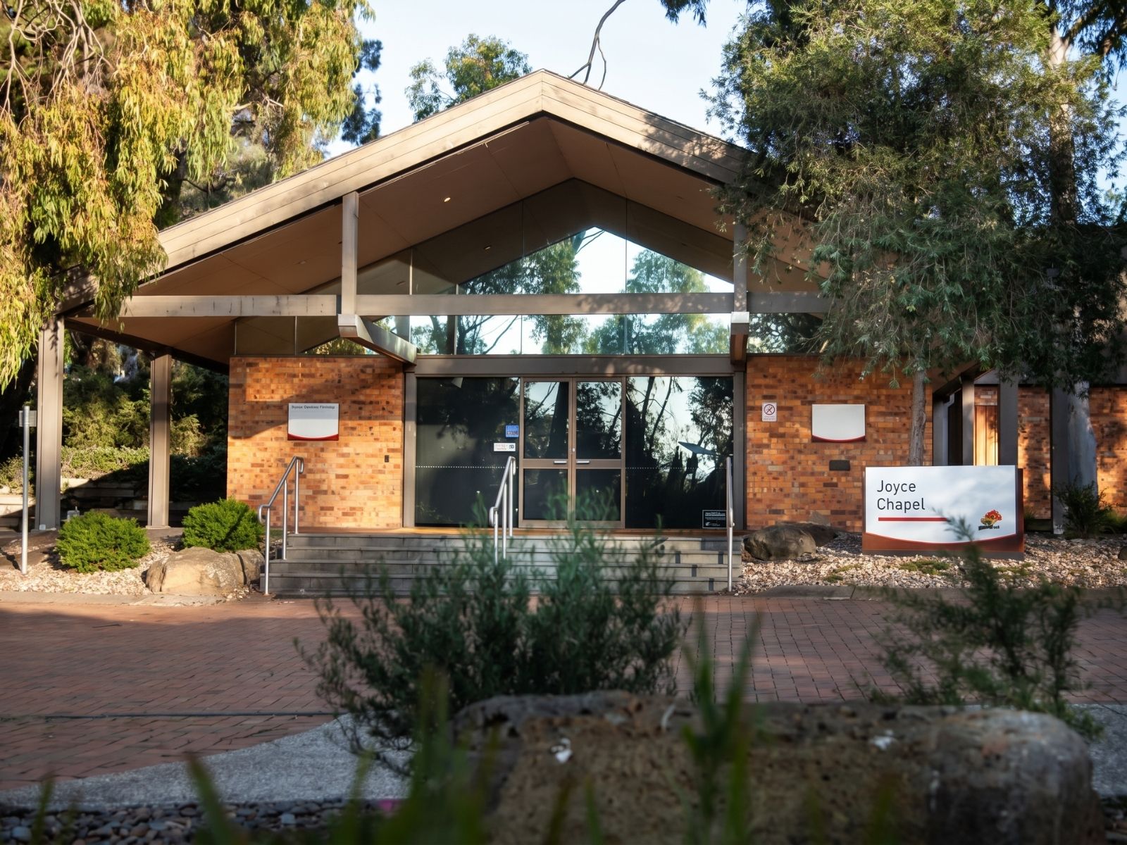 Joyce Chapel exterior at Fawkner Memorial Park, winged roof and brick entry beneath eucalyptus trees