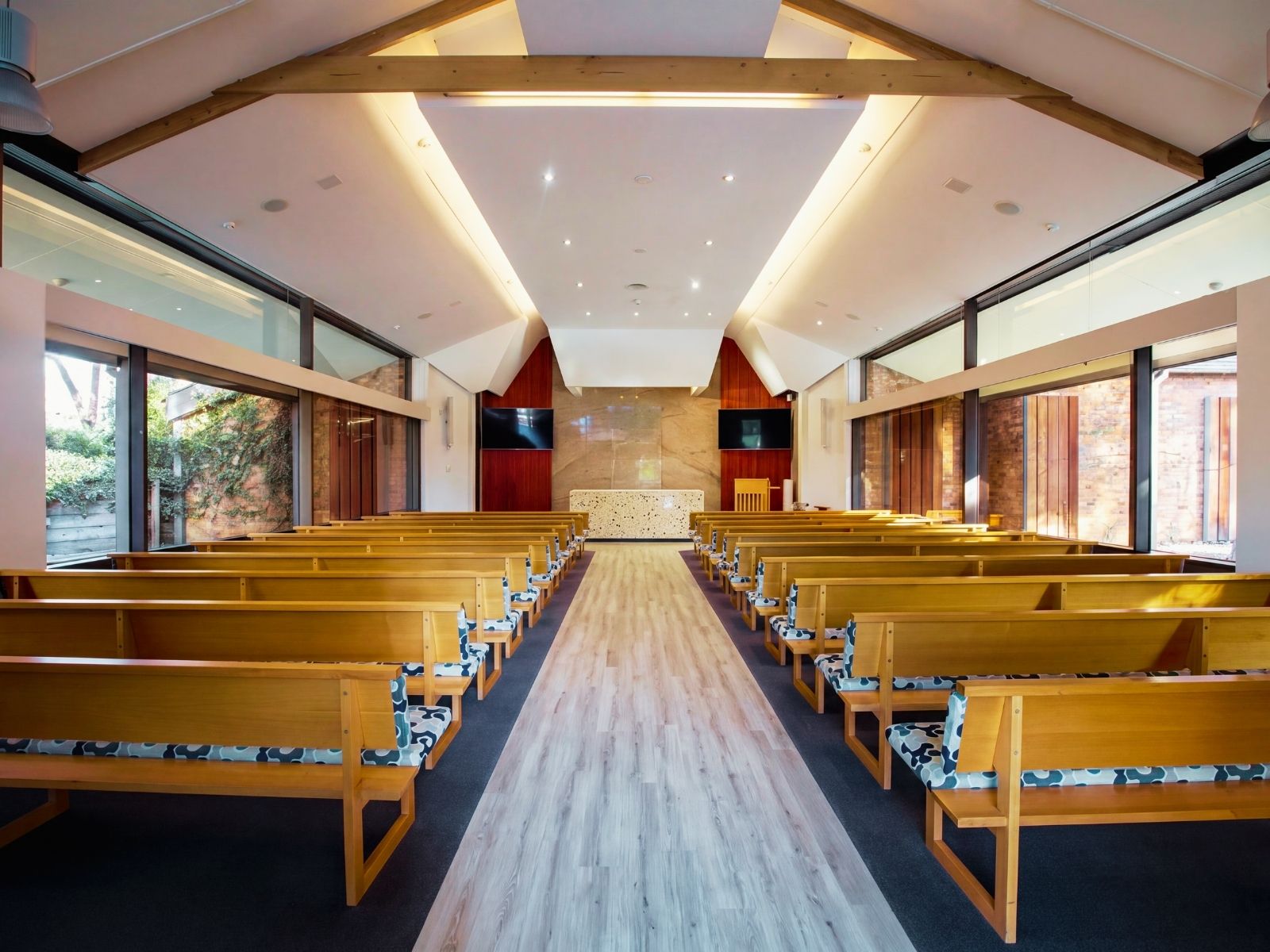 Timber pews and terrazzo catafalque inside Joyce Chapel beneath the raked ceiling