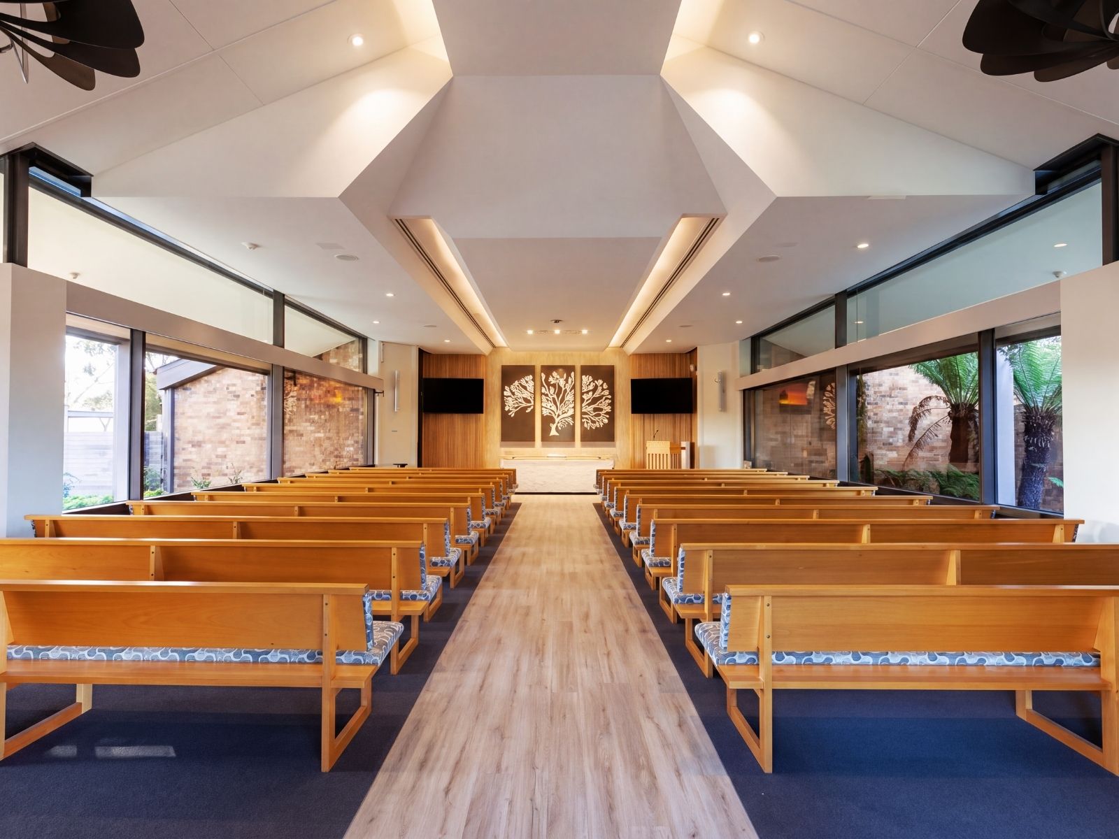 Timber pews lining the aisle to the catafalque and tree artwork inside Cordell Chapel
