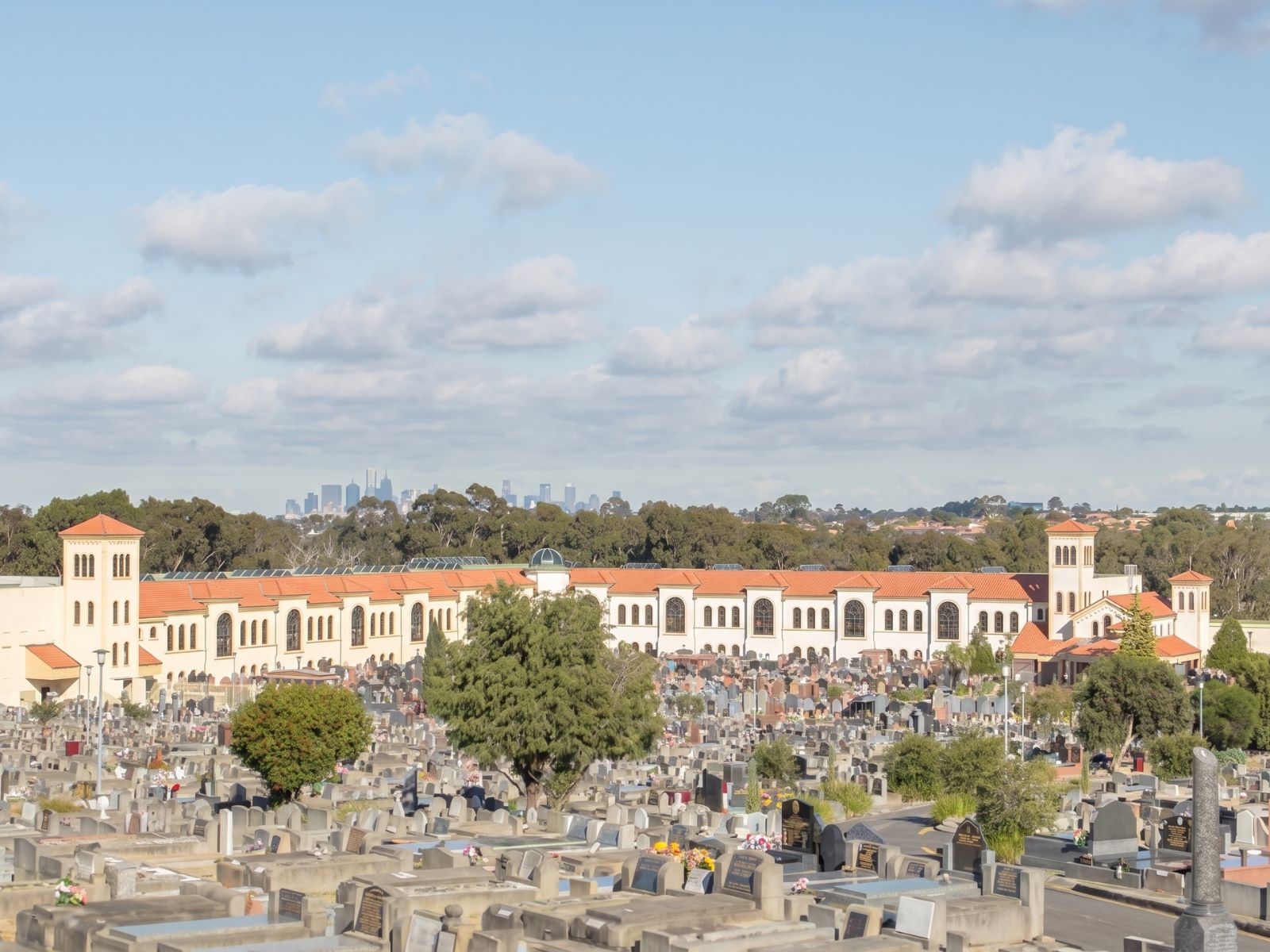 Preston Cemetery mausoleum complex with terracotta roofs and towers, Melbourne skyline beyond