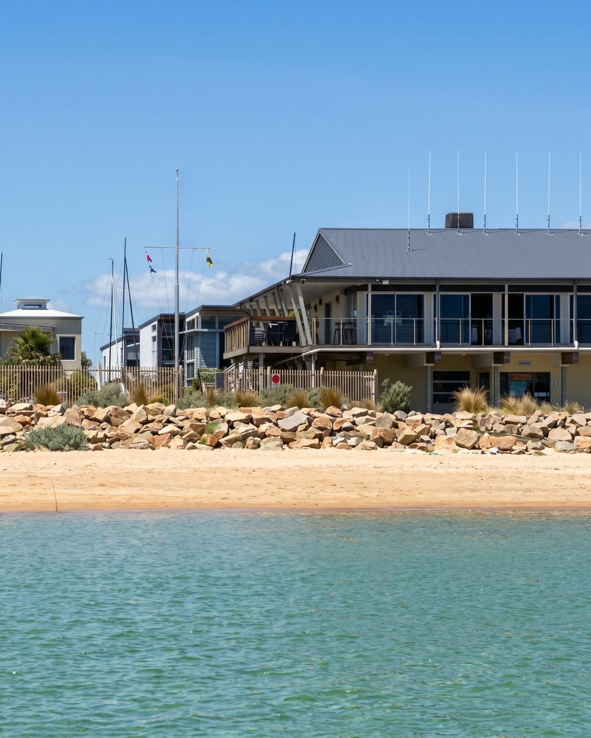 Safety Beach Sailing Club clubhouse on the foreshore, seen across calm water from the beach