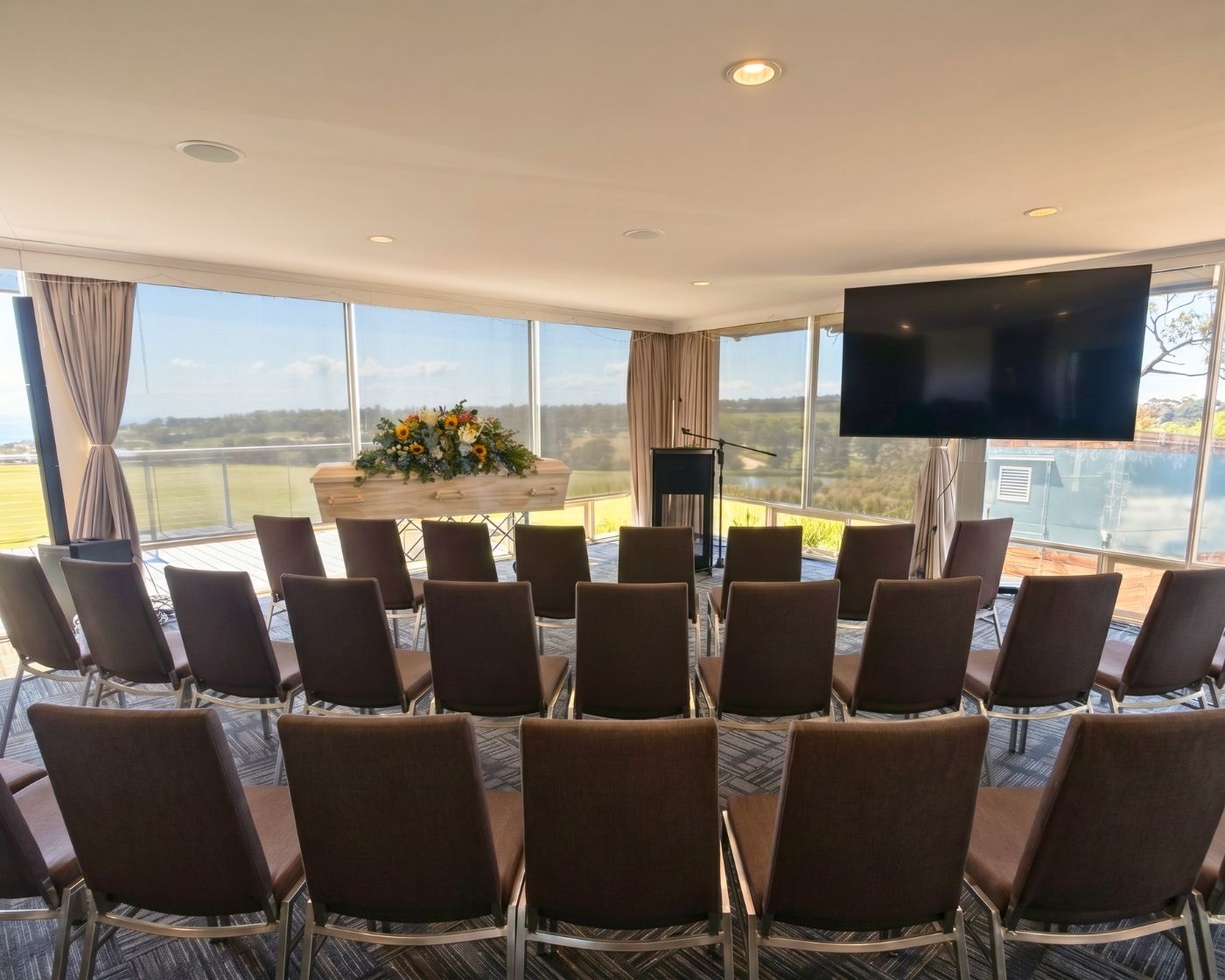 The Tallis Room set with rows of chairs for a funeral service, windows to the fairways and bay
