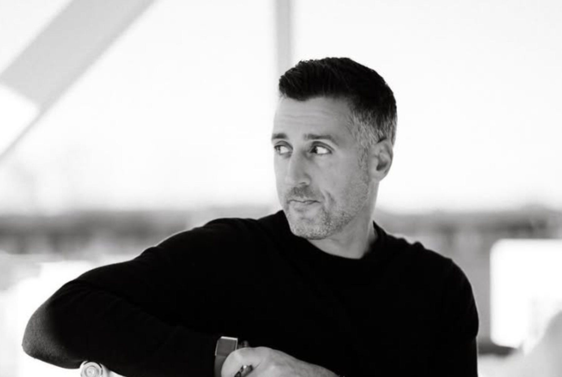 Black-and-white portrait of a man in a black shirt looking thoughtfully to the side.
