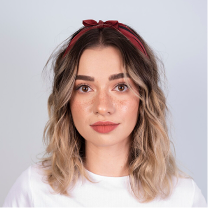 Bigsite employee with wavy blonde hair wearing red headband and white shirt against gray background.