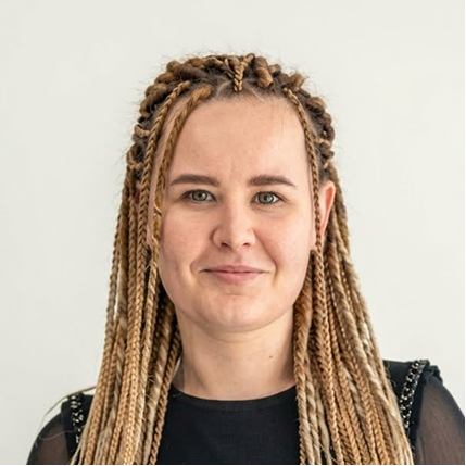 Portrait of a bigsite employee with long braided hair wearing a black top, smiling slightly against a white background.