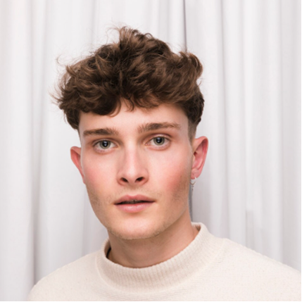 Close-up of a bigsite employee with curly brown hair wearing a cream turtleneck in front of a white curtain.