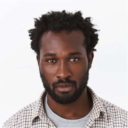 Serious young man with a beard and short curly hair wearing a checkered shirt over a gray tee.