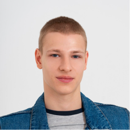 Portrait of a young man with short hair wearing a denim jacket over a striped shirt against a white background.
