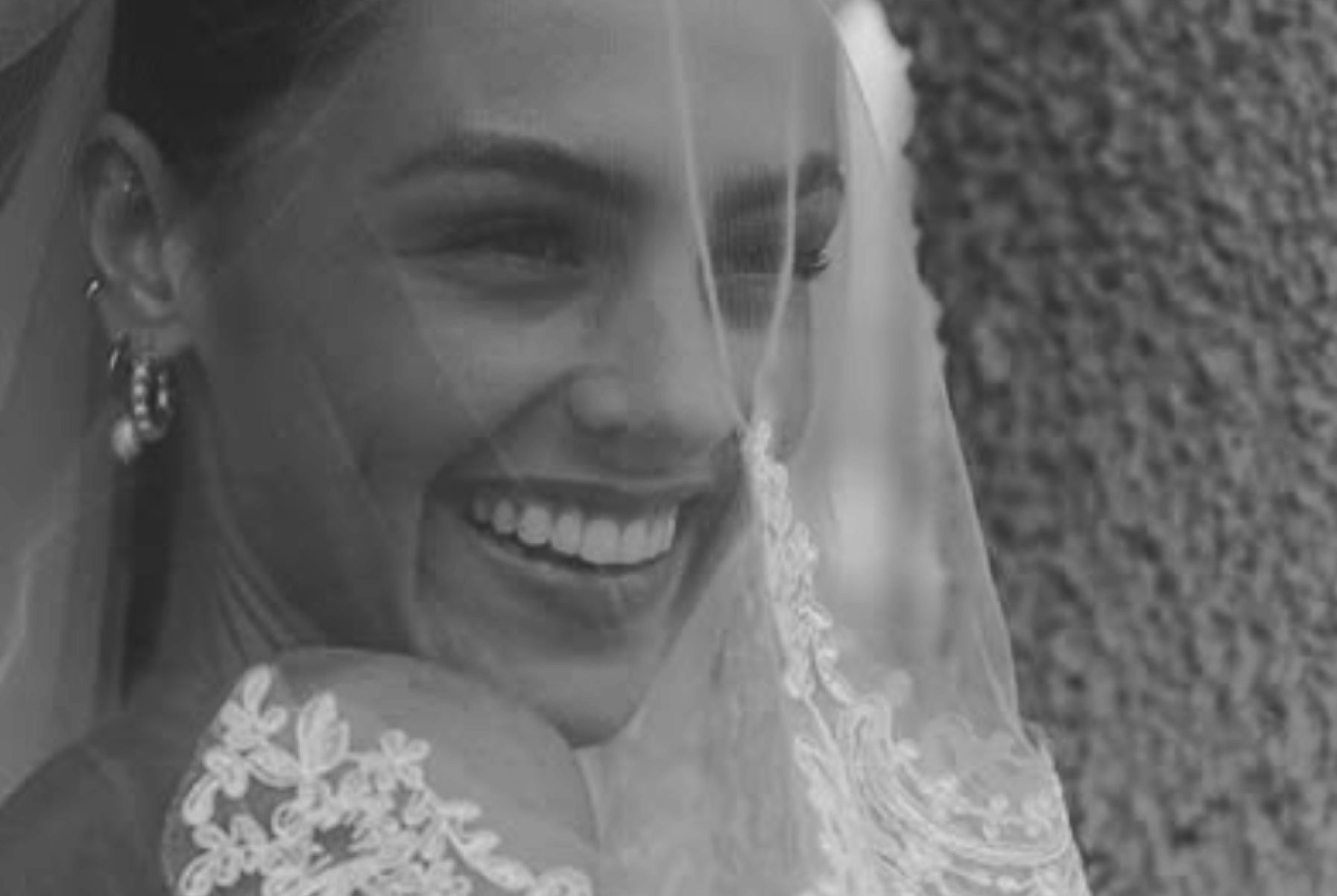 Close-up of a smiling bride with earrings and a lace veil over her face.