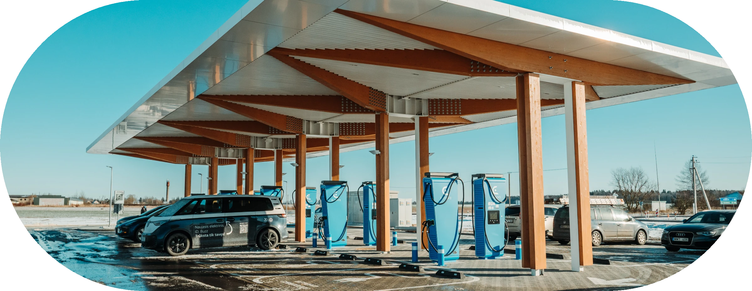 Eldrive charging hub in Raseiniai: wooden canopy over blue Eldrive fast chargers