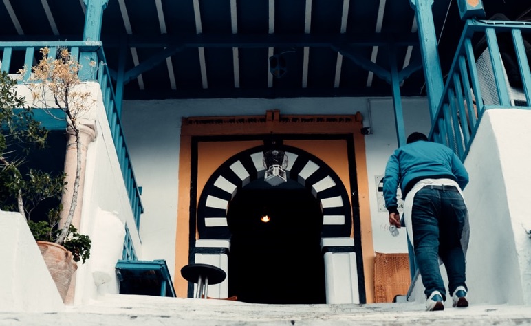 Person walking up steps toward entrance with black and white arched doorway and blue railings.