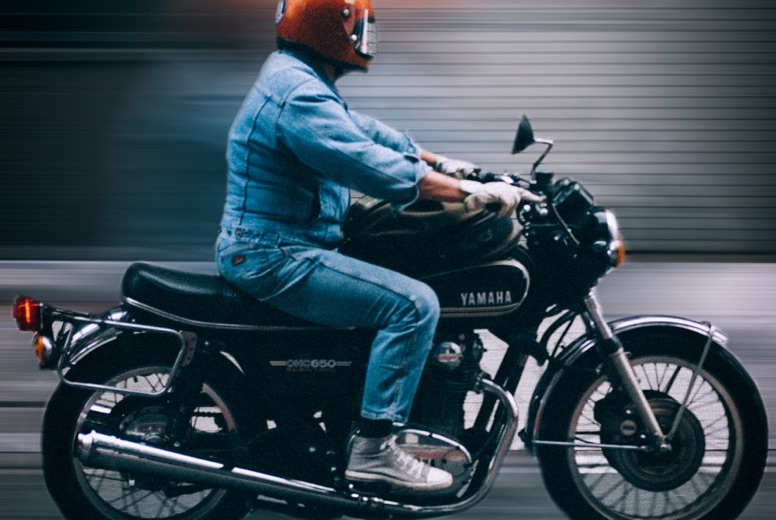 Person in orange helmet and denim jacket riding a black Yamaha motorcycle on a blurred background.