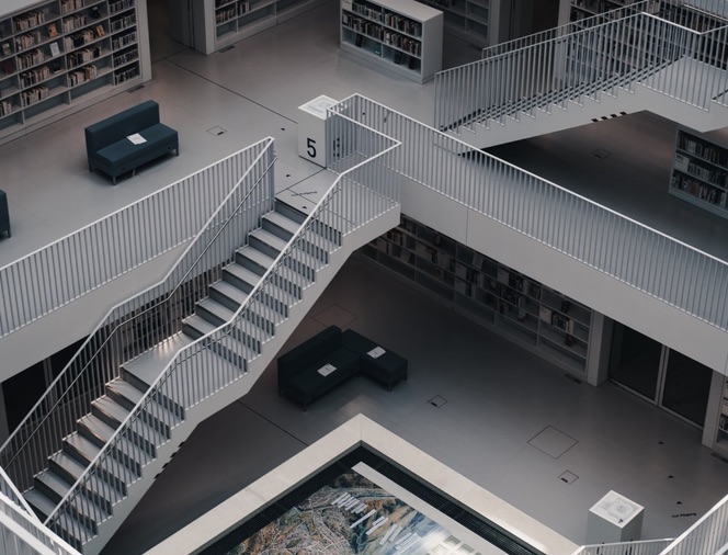 Modern library interior with white metal staircases, bookshelves, and dark seating areas.