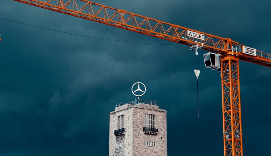 Orange construction crane above a stone tower with a large Mercedes-Benz star emblem on top.