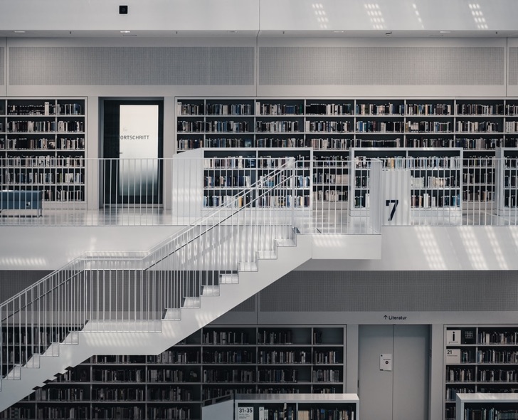 Modern library interior with white staircases and shelves full of books on two levels.
