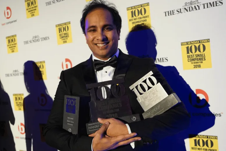 Smiling man in tuxedo holding multiple Sunday Times 100 awards for best small companies.