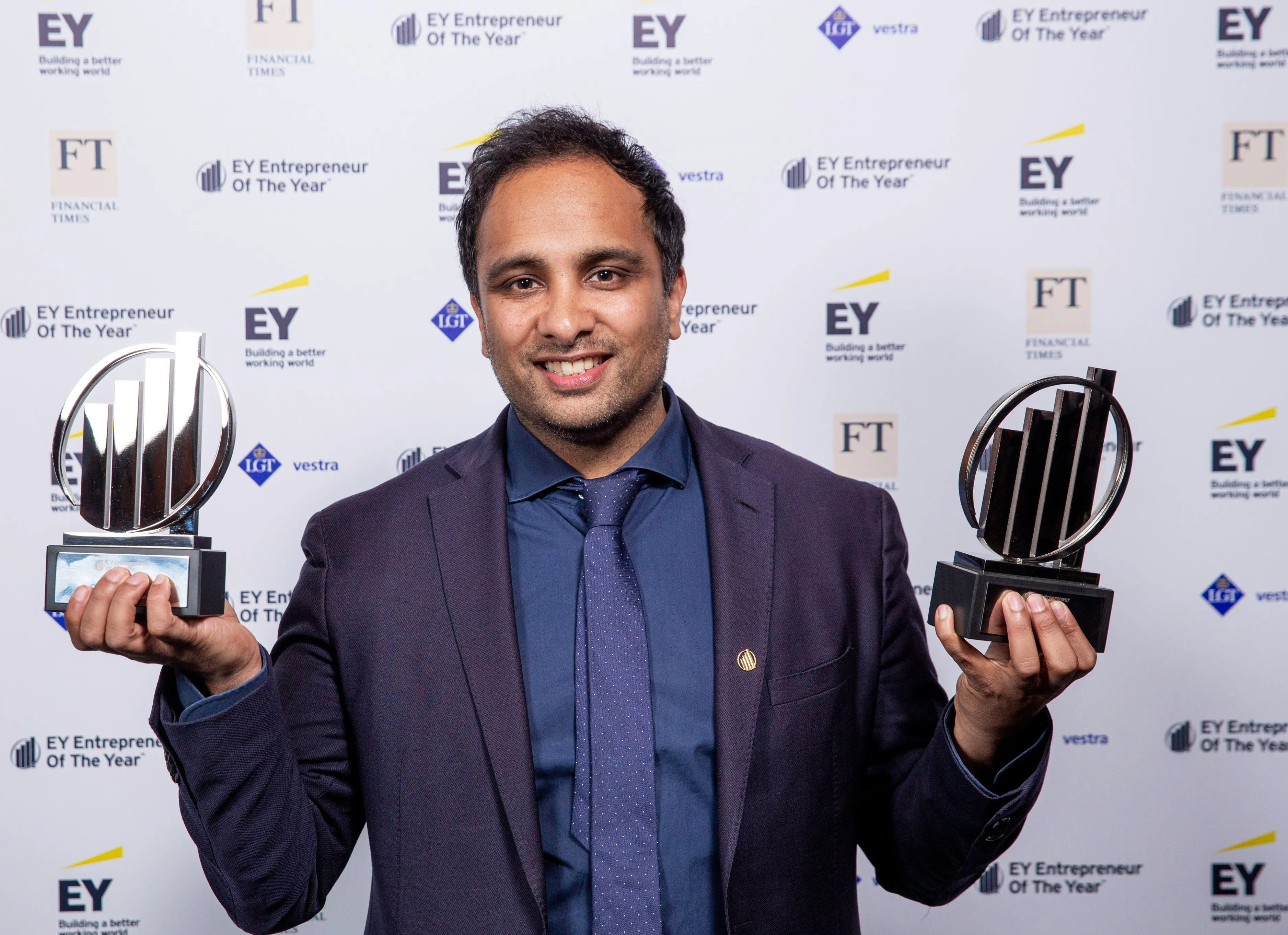 Man in suit smiling and holding two awards at an EY Entrepreneur of the Year event.