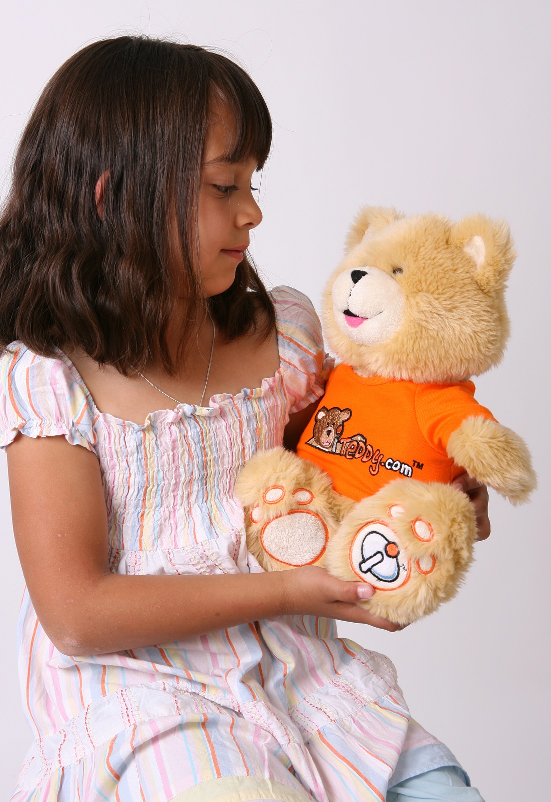 Young girl holding an iTeddy teddy bear while smiling at it.