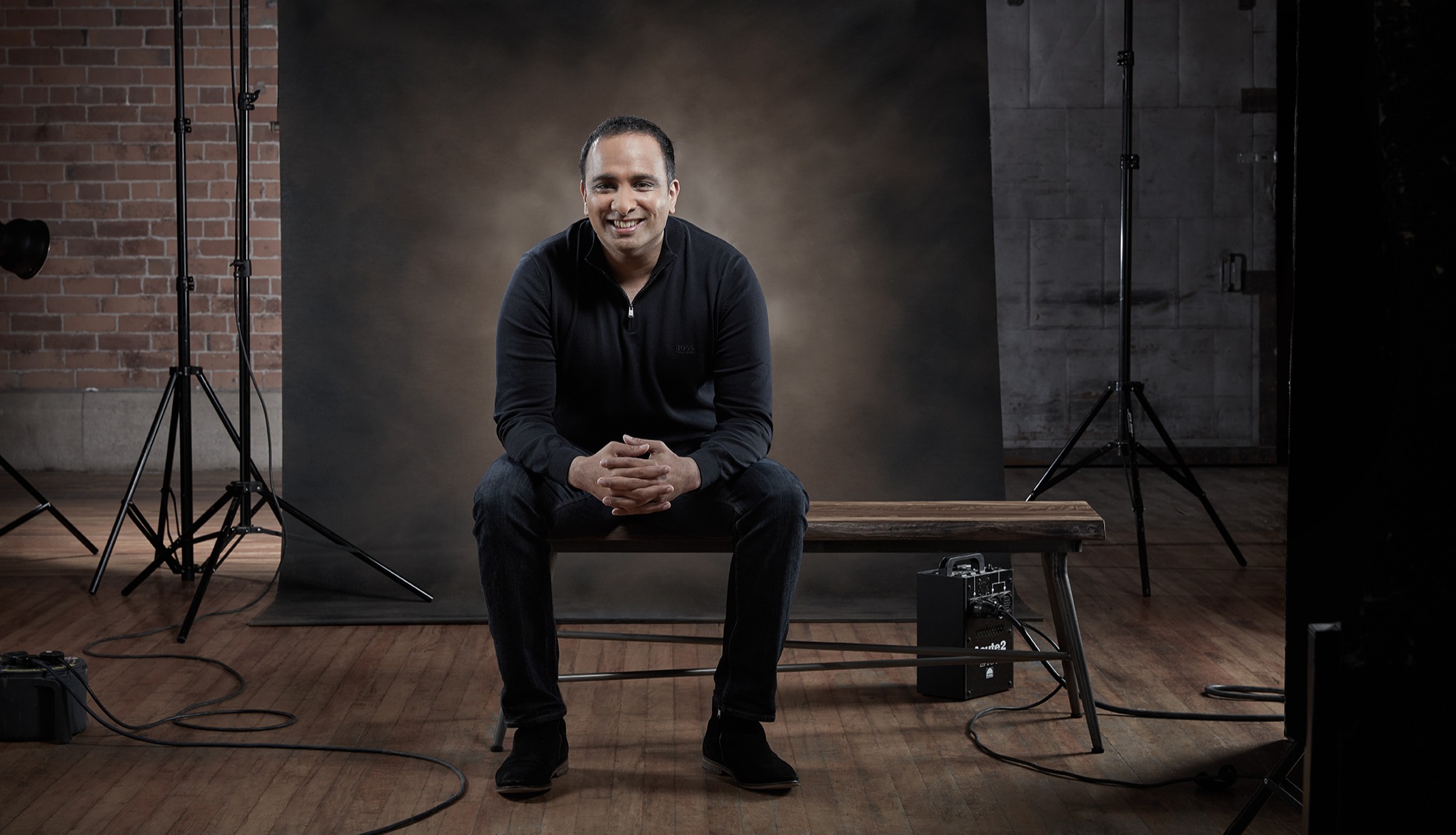 Portrait of Imran Hakim seated in a photography studio with a relaxed pose.