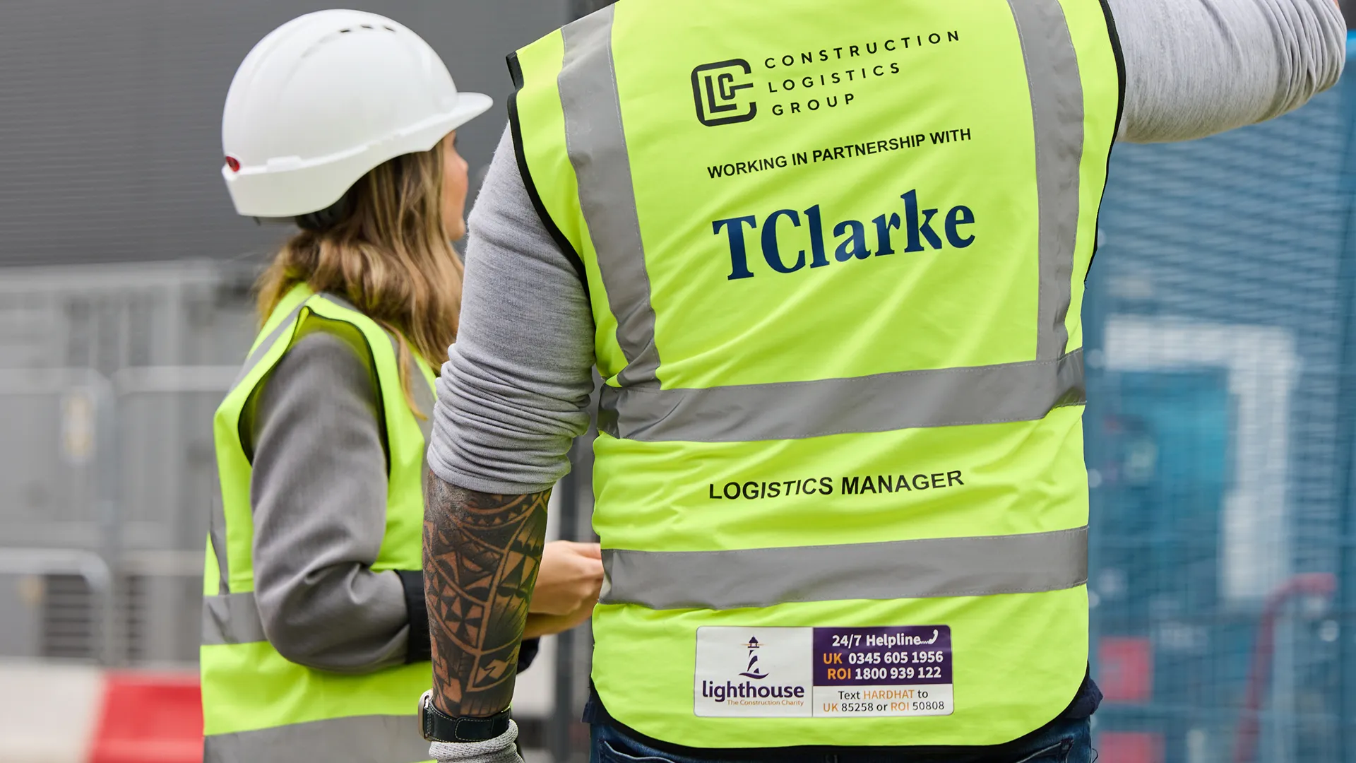 Two construction workers wearing high-visibility vests and one in a white hard hat standing at a construction site.