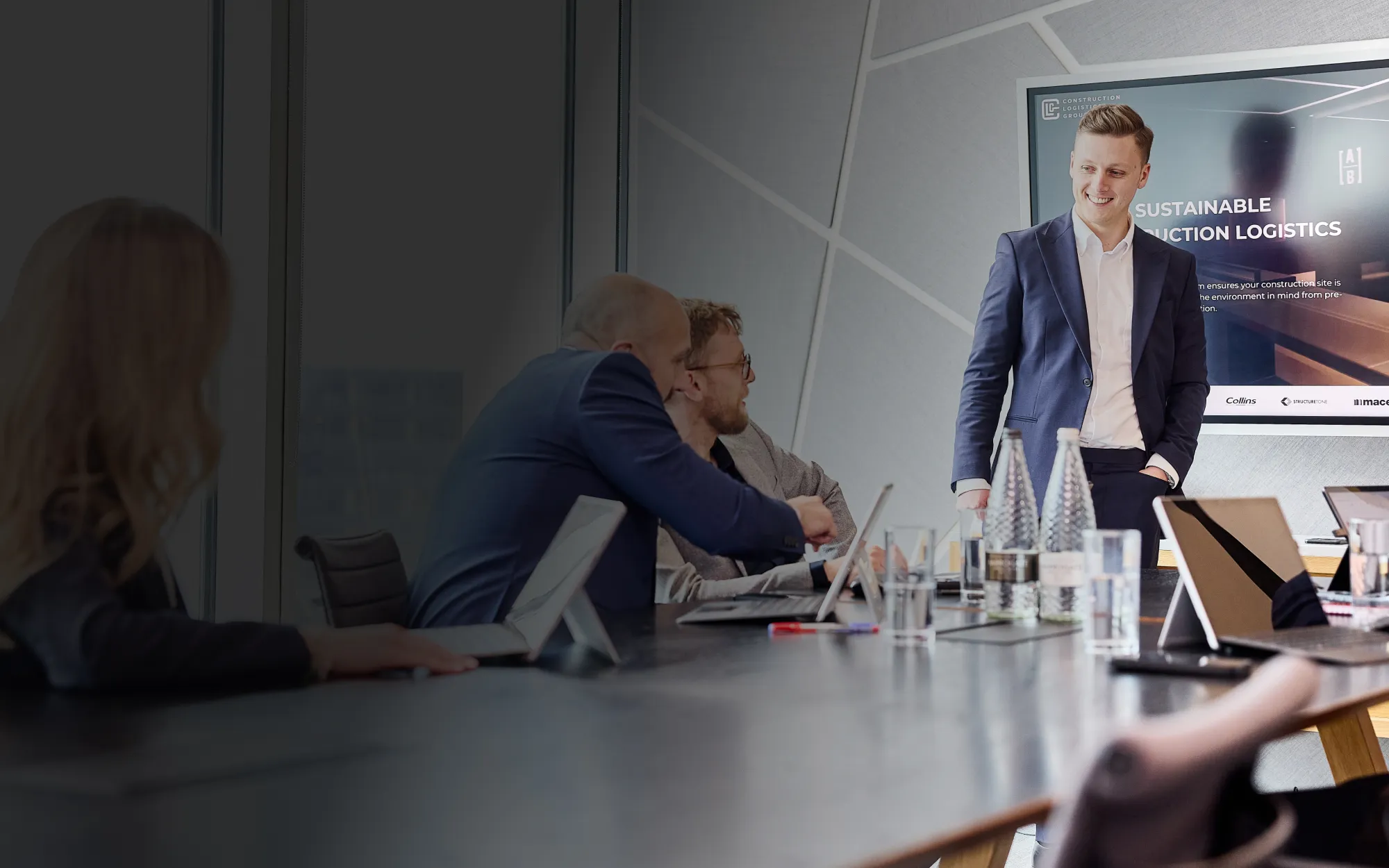 Businessman in a blue suit presenting sustainable construction logistics to colleagues in a modern meeting room.