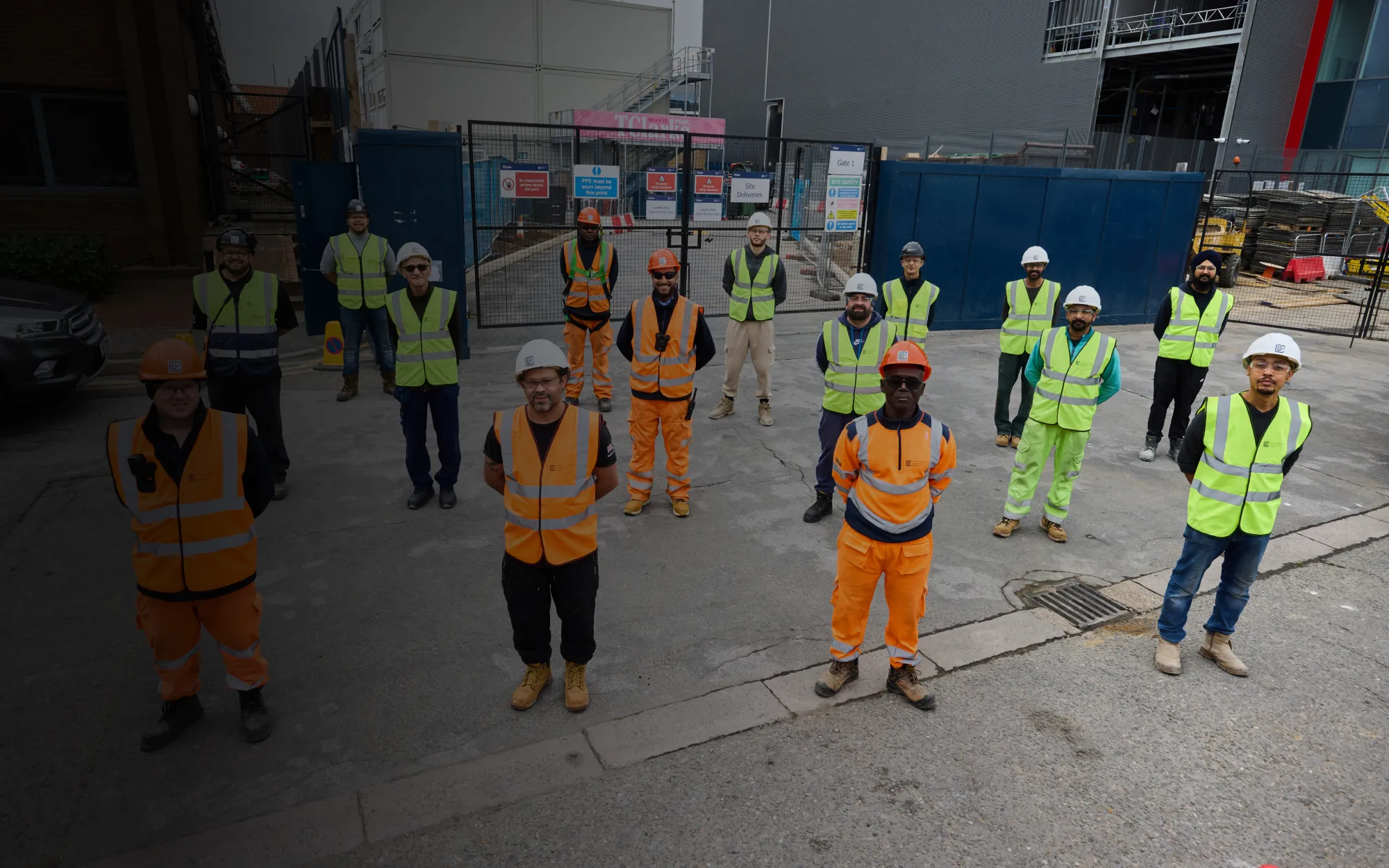 Group of construction workers wearing helmets and high-visibility vests standing outdoors on a construction site.