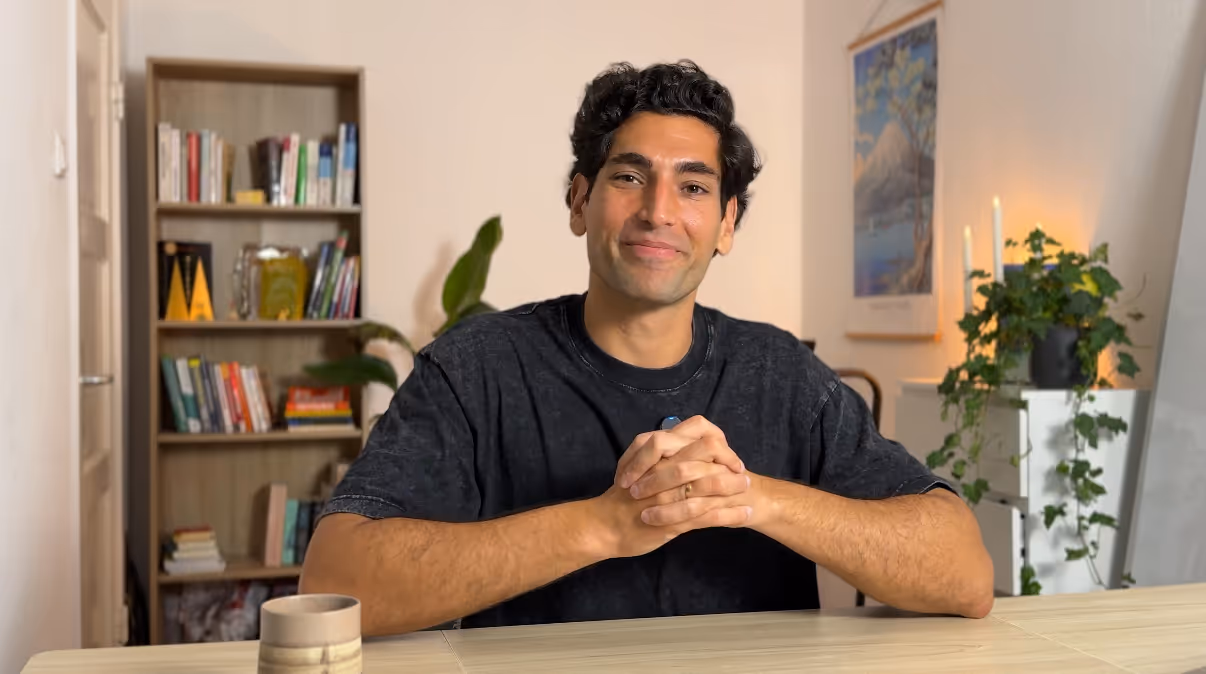 Gino sitzt lächelnd am Tisch und erklärt die Vorteile der Coaching Community. Davor ist ein Play-Button zu sehen.