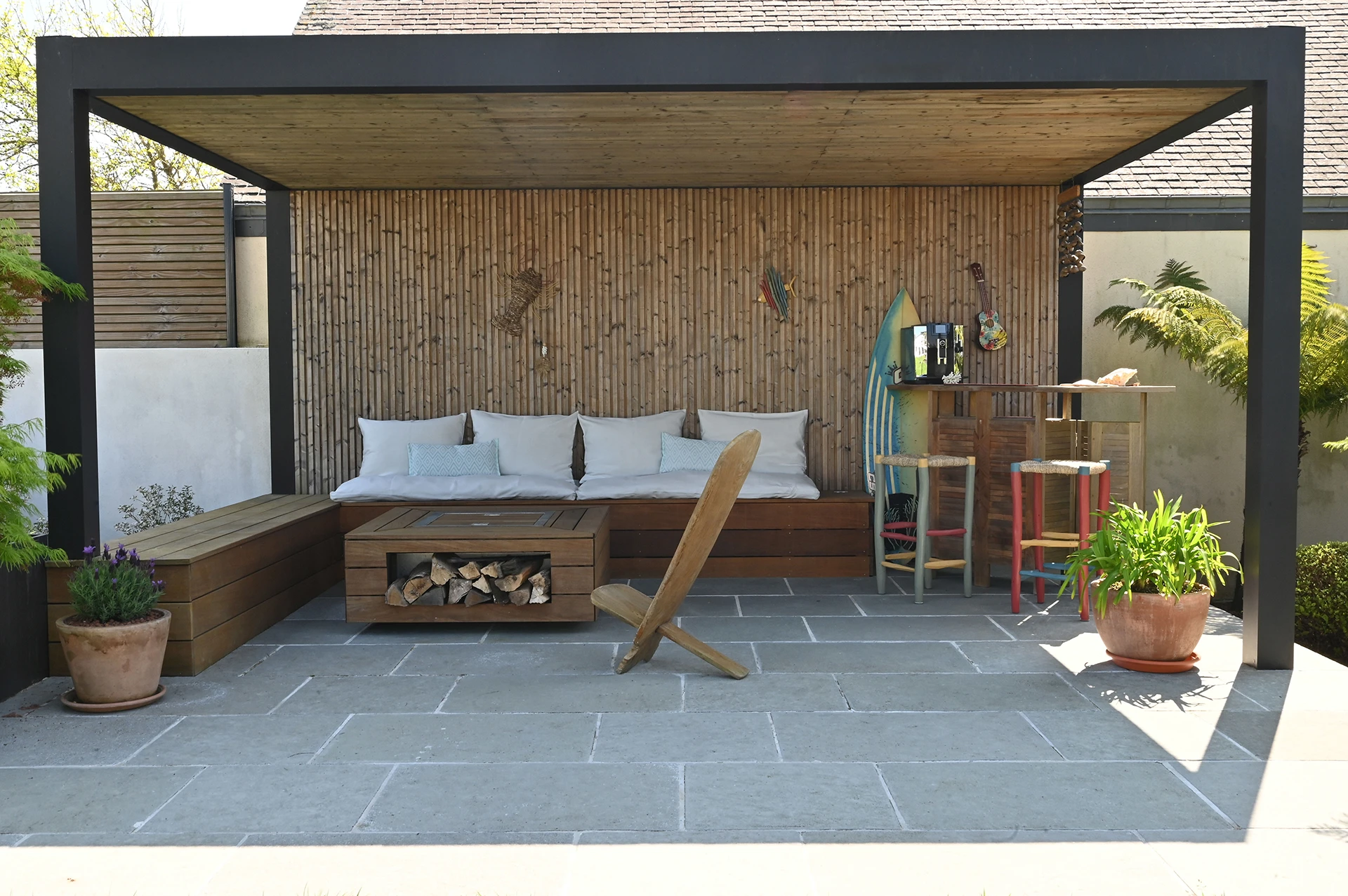 Détail de la pergola Maluwi en aluminium gris anthracite avec fond en lames de bois, intégrée dans un jardin paysager à Plouhinec.