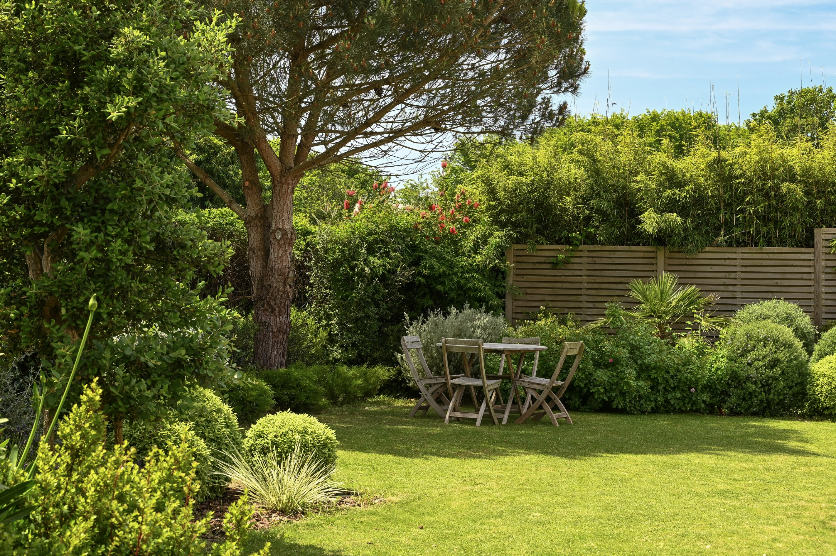Jardin végétalisé avec des plantes de différentes hauteurs qui ombrage un salon de jardin à Plouhinec