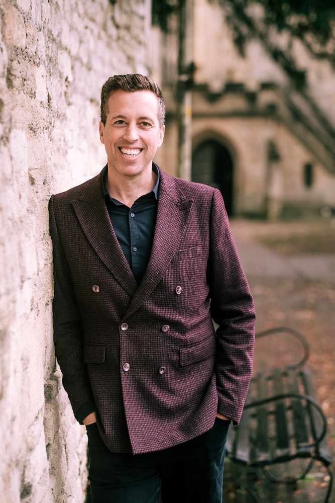 Mid shot of Warren wearing a purple blazer and navy blue shirt
