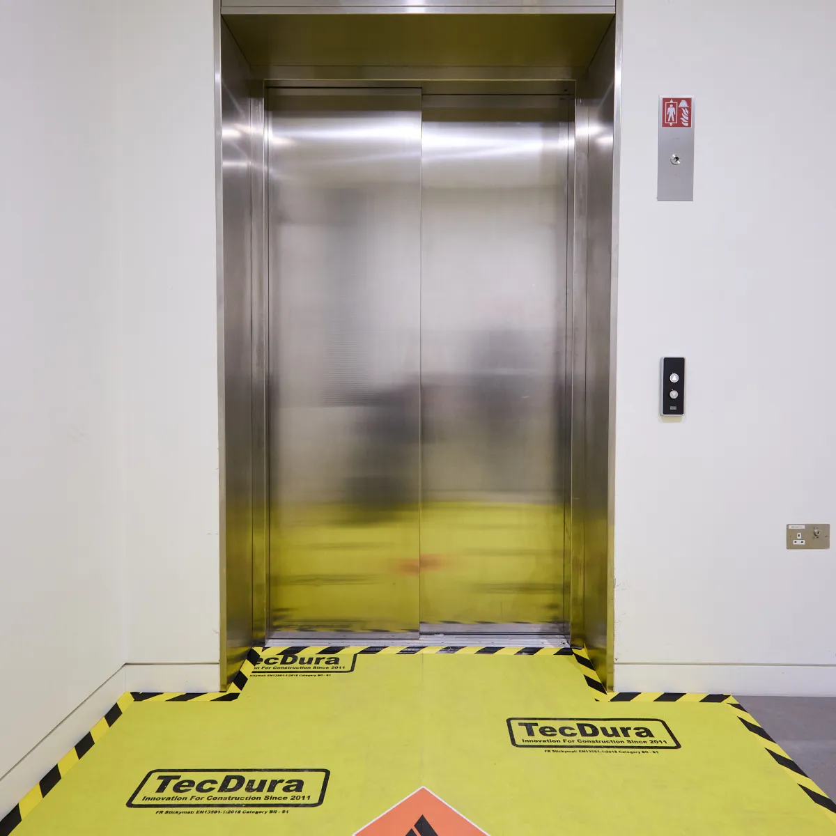 Lift interior with yellow protective flooring and safety markings.