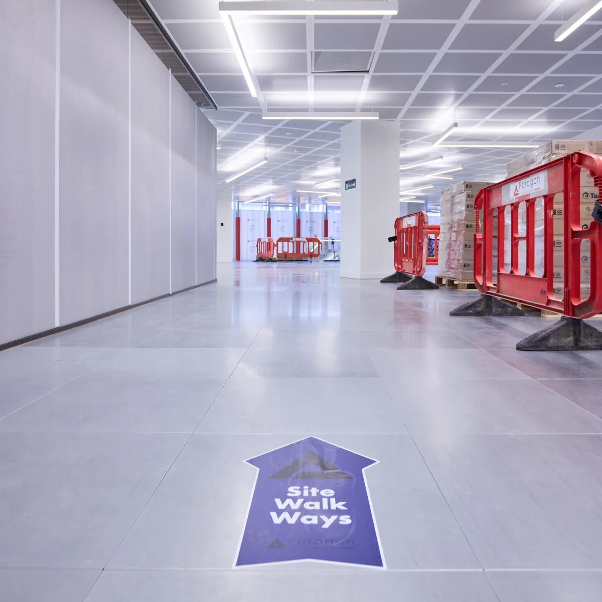 Bright corridor under refurbishment with red barriers and a directional floor arrow.