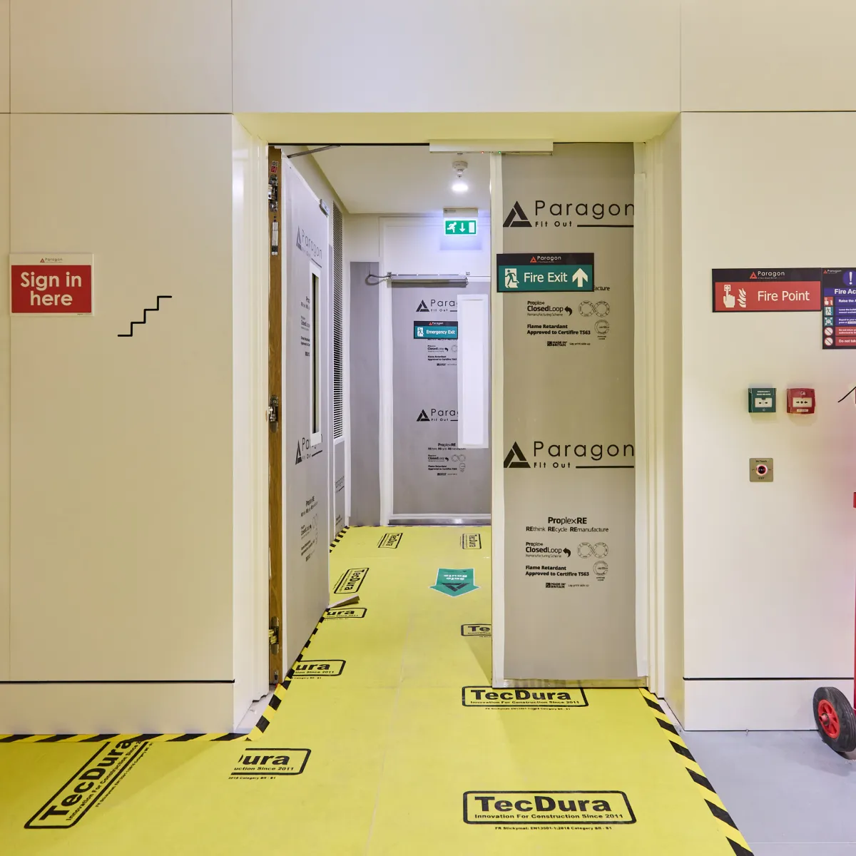 Temporary site doorway with safety signage and yellow protective floor covering.