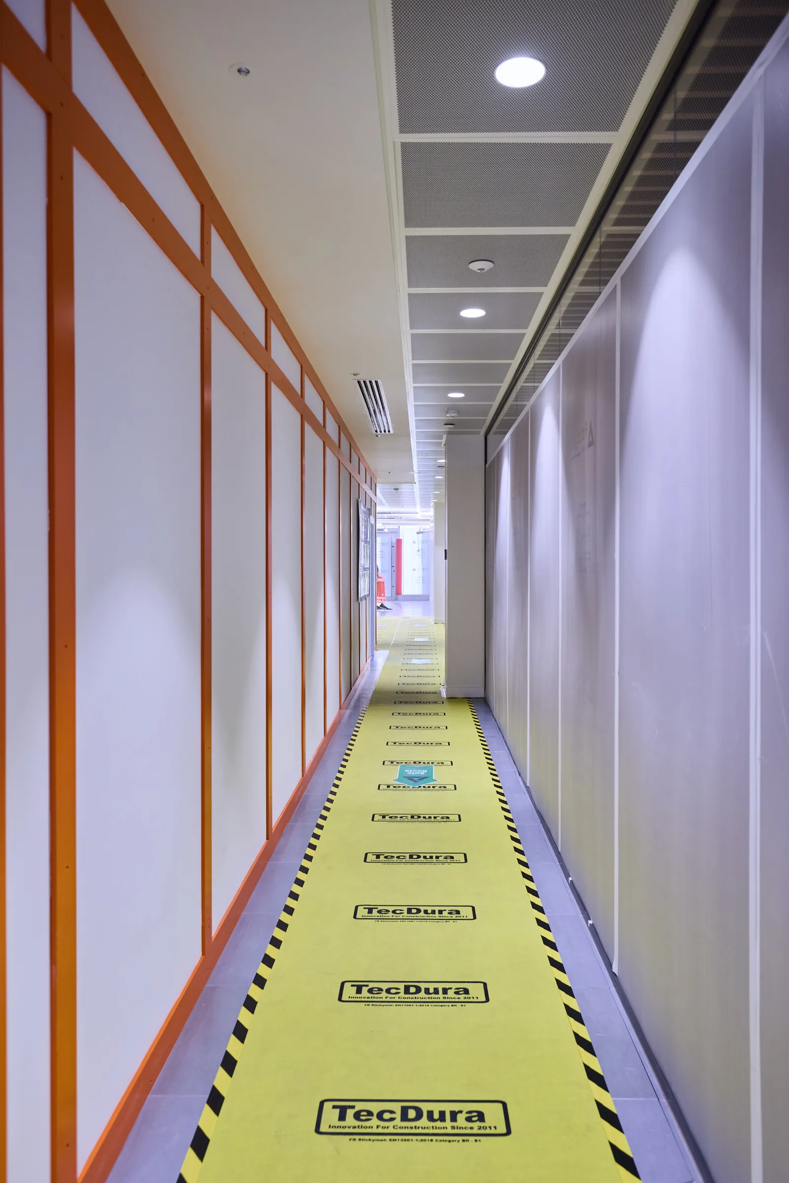 Narrow temporary corridor with orange framing and yellow protective floor covering.