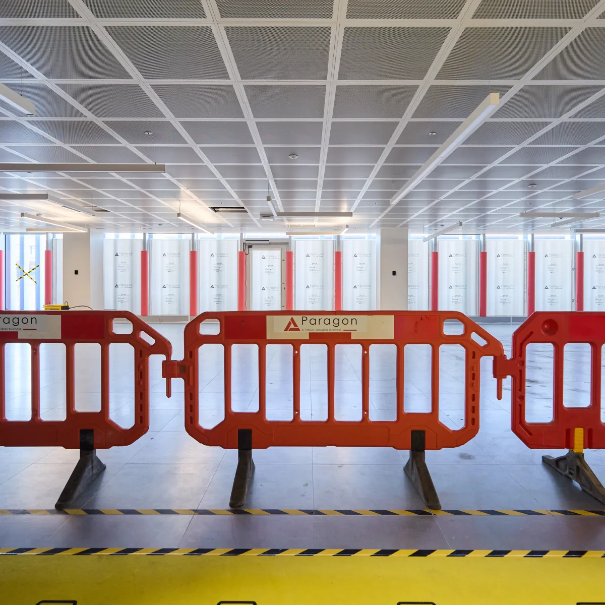 Refurbishment area enclosed by orange safety barriers beneath a suspended ceiling.