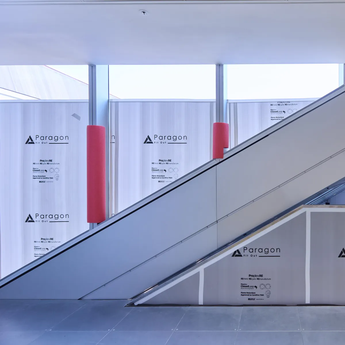 Escalator passing in front of temporary construction hoarding and covered windows.