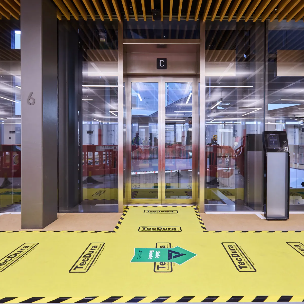 Lift lobby under refurbishment with yellow protective flooring and safety markings.