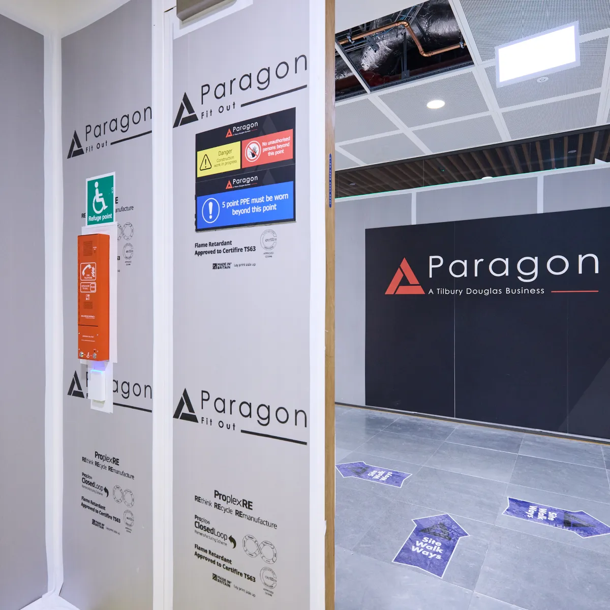 Construction site entrance with Paragon branding and safety information displayed on temporary hoarding.