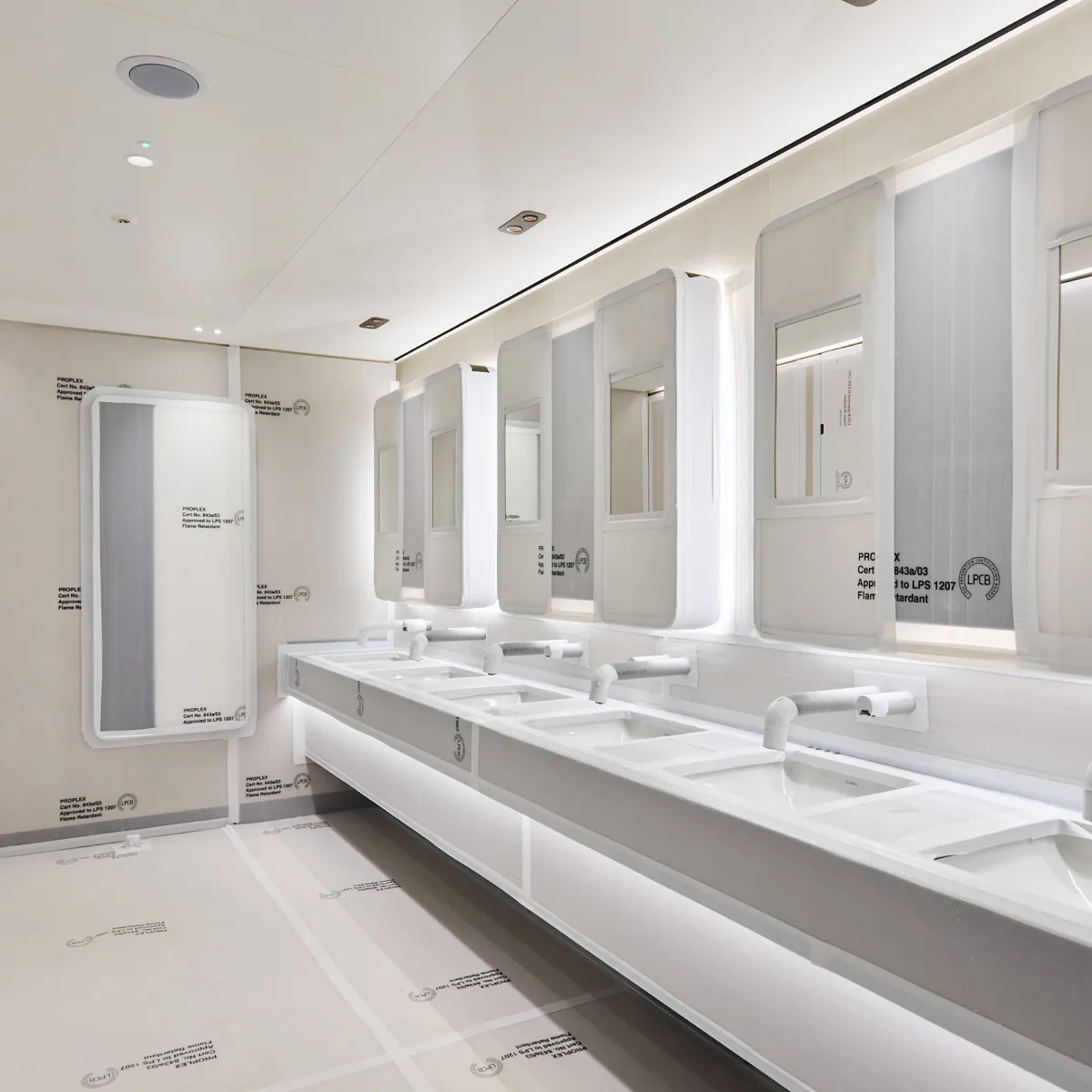 Modern white washroom with a row of sinks, mirrors and cubicles.