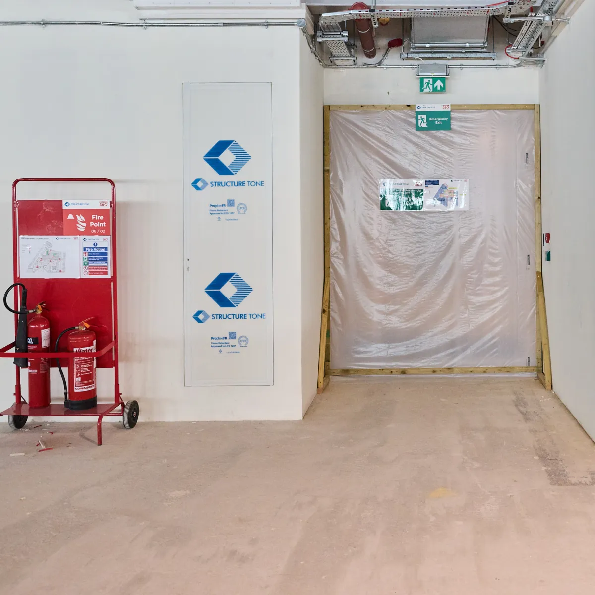 Fire extinguishers beside a temporarily sealed doorway on a construction site.